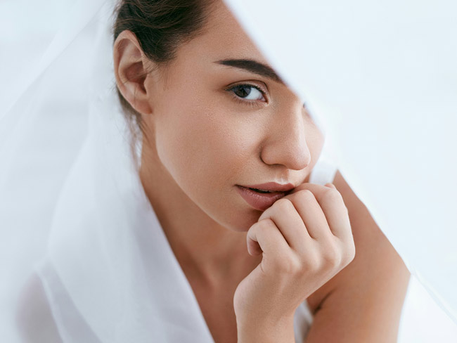 Eine Frau umhüllt von weißen Tüchern schaut direkt in die Kamera.