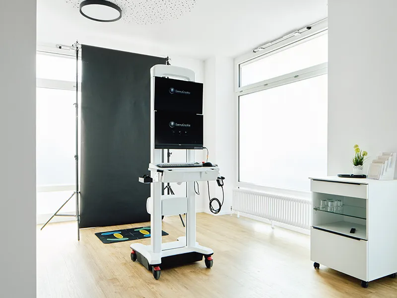 Hochtechnologisches medizinisches Total Body Mapping Gerät auf Rollen vor schwarzem Hintergrund in heller Hautarztpraxis mit großem Fenster und weißem Schrank