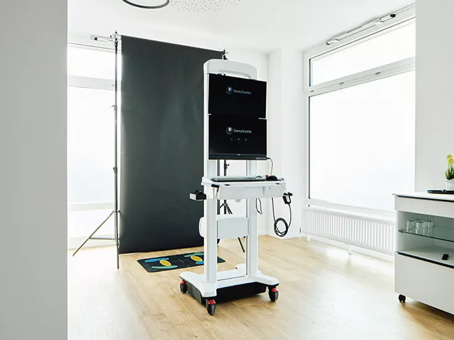 Hochtechnologisches medizinisches Total Body Mapping Gerät auf Rollen vor schwarzem Hintergrund in heller Hautarztpraxis mit großem Fenster und weißem Schrank